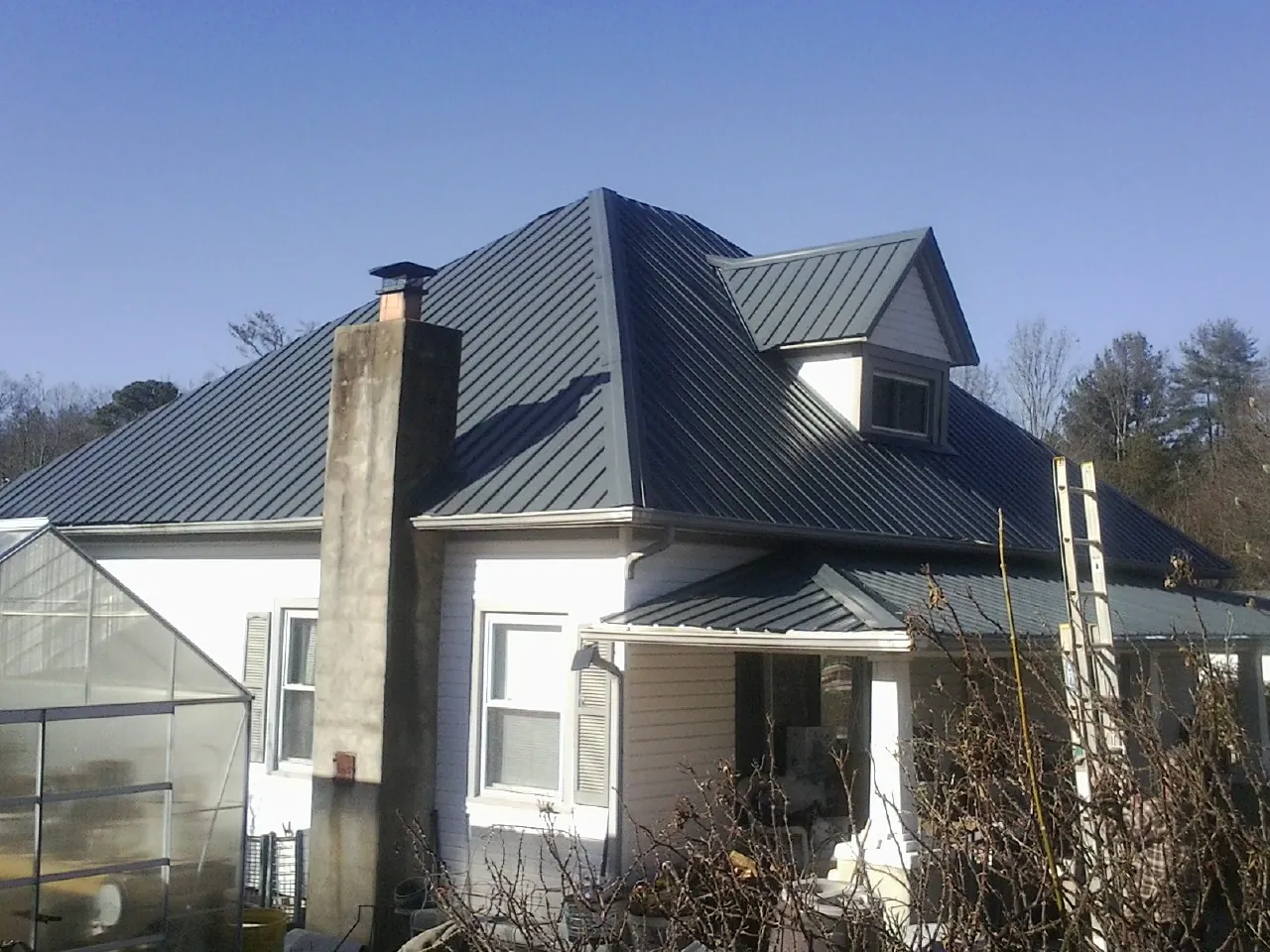 Dark blue standing seam metal roof on a white farmhouse with dormer — Slate & Tile Roof Repair by Roofing Brothers in Middlebrook