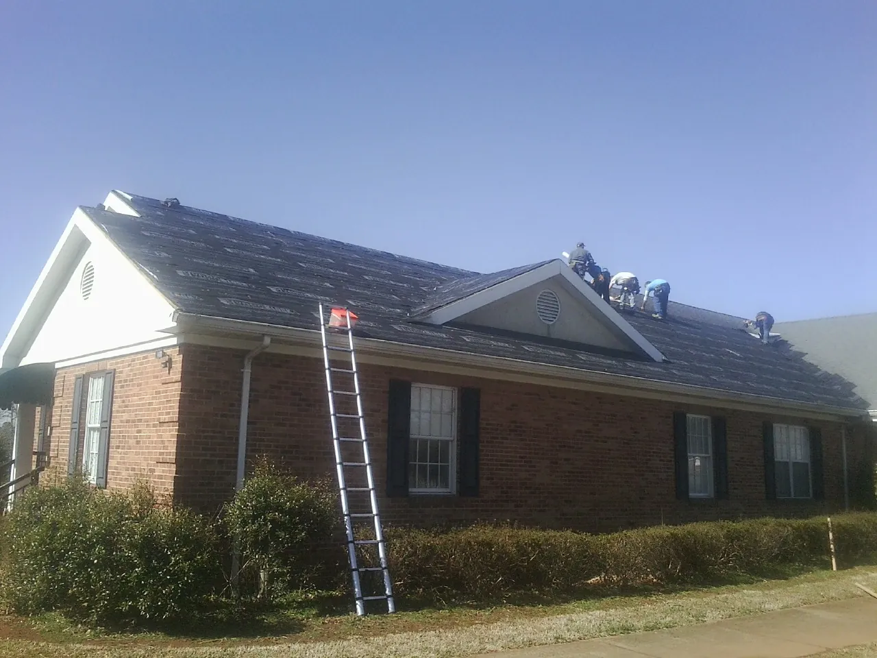 Crew tearing shingles off a brick ranch roof with a ladder set — Emergency Roof Repair work by our crew in Middlebrook