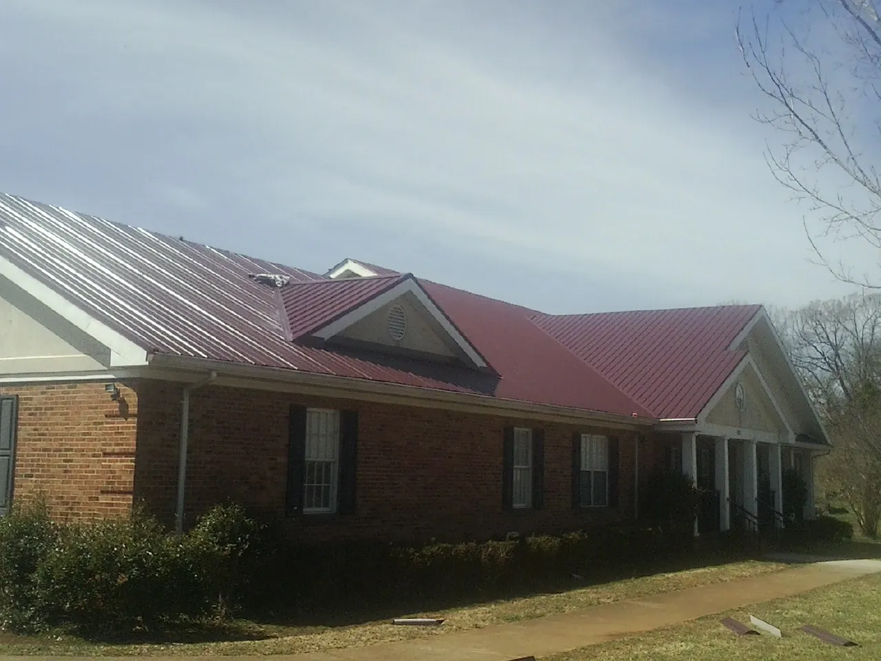 Red metal roof with gabled entries on a long brick building, from a Hail Damage Roof Repair job in Middlebrook