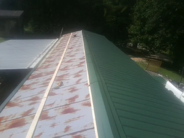 Old rusted panels beside newly installed green metal roofing — Wind Damage Roof Repair by Roofing Brothers in Middlebrook