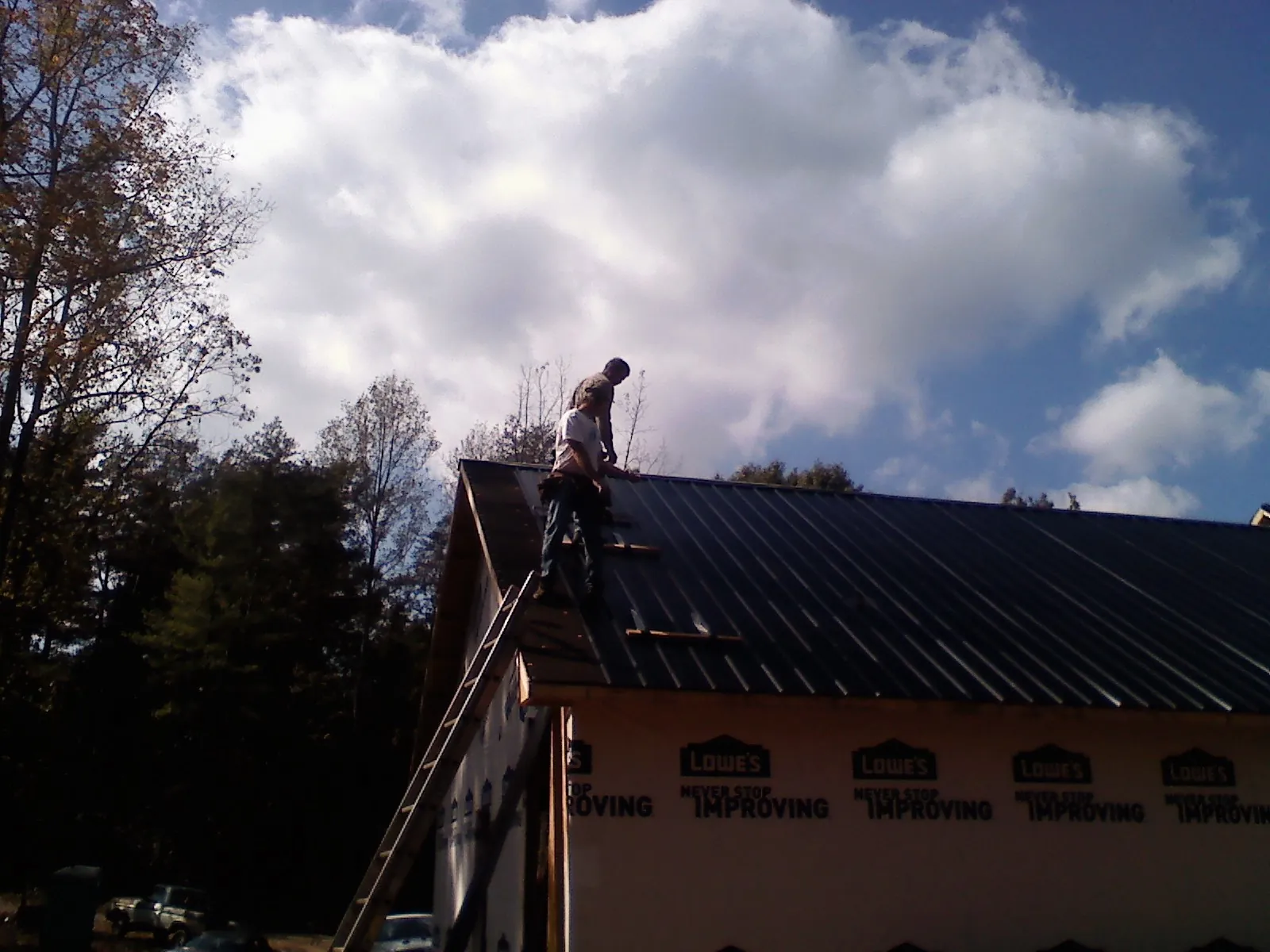 Roofer fastening dark metal panels high against a cloudy sky, from a Roof Inspection job in Middlebrook